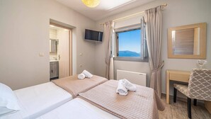 Ein Hotelzimmer mit zwei Betten, einem Fernseher, einem Fenster mit Vorhängen, einem Schreibtisch und einem Sessel.