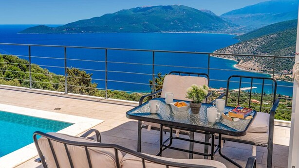 Ein Balkon mit Glastisch, Stühlen und Blick auf Meer und Berge.