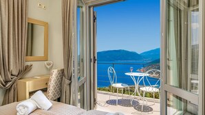 Ein Hotelzimmer mit Bett, Nachttisch, Spiegel und Blick auf einen Balkon mit Sitzgelegenheit und einen malerischen See.