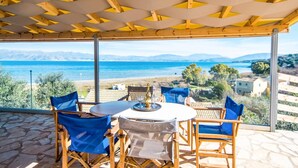 Un espace extérieur aménagé, abrité et doté de tables et de chaises, offrant une vue panoramique sur la mer et les montagnes.