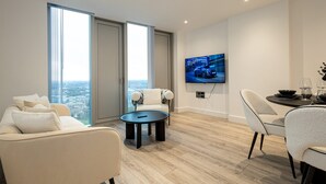 A modern living room with a sofa, a dining table with chairs, a coffee table, and a TV mounted on the wall displaying a car advertisement. - Nuvola Suite by Casacity (Manchester)