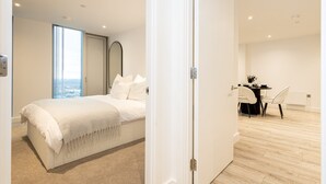 A modern bedroom with a large bed, a view of the ocean, a dining area with a table and chairs, and a minimalist design. - Nuvola Suite by Casacity (Manchester)