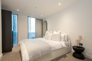 Quarto moderno com uma cama grande, mesa de cabeceira e vista através de uma janela ampla.
