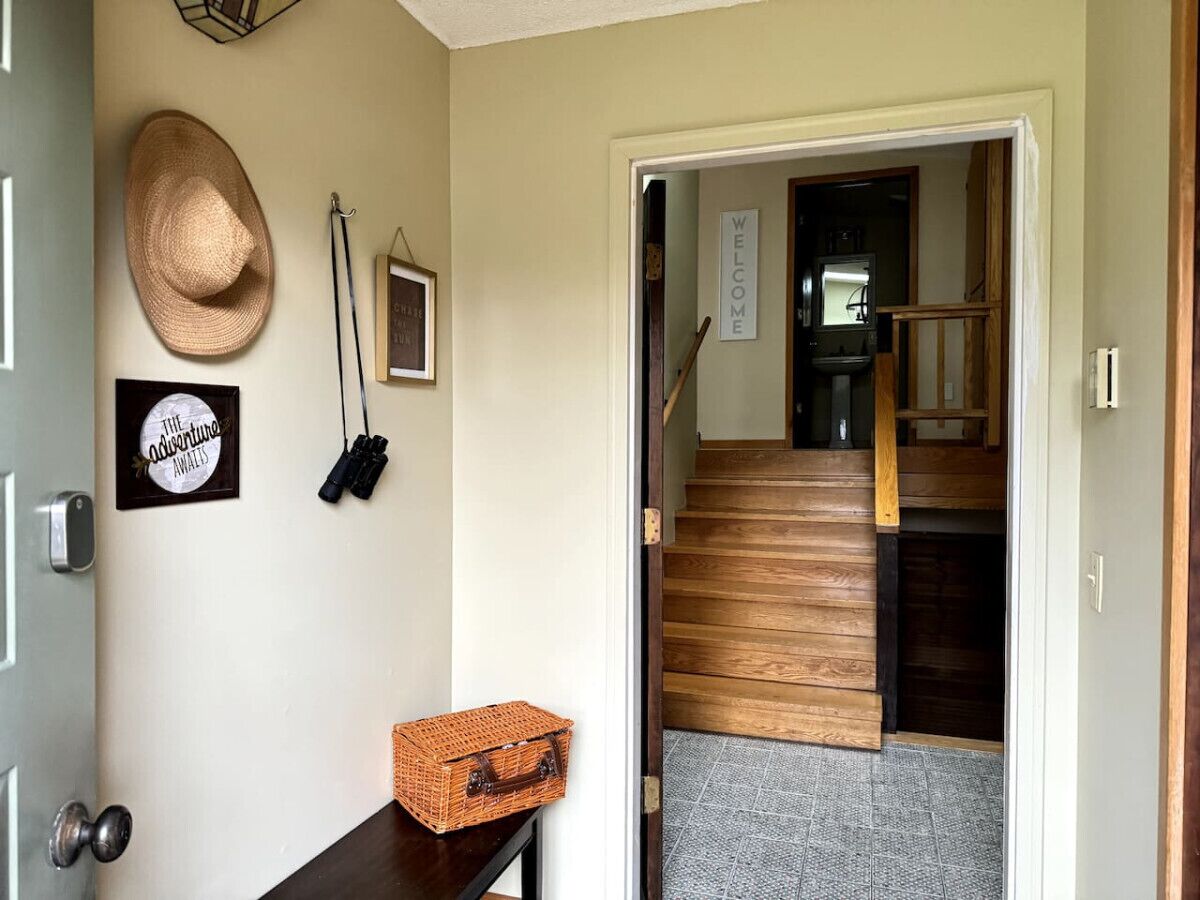 Un couloir avec un escalier en bois, un panier en osier et un chapeau accroché au mur.