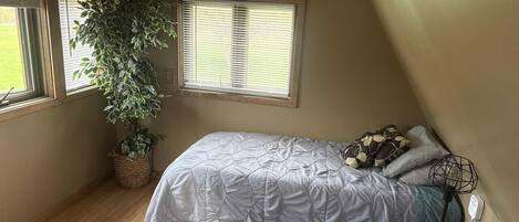 Un dormitorio con cama, planta en maceta, ventana y mesita de noche.