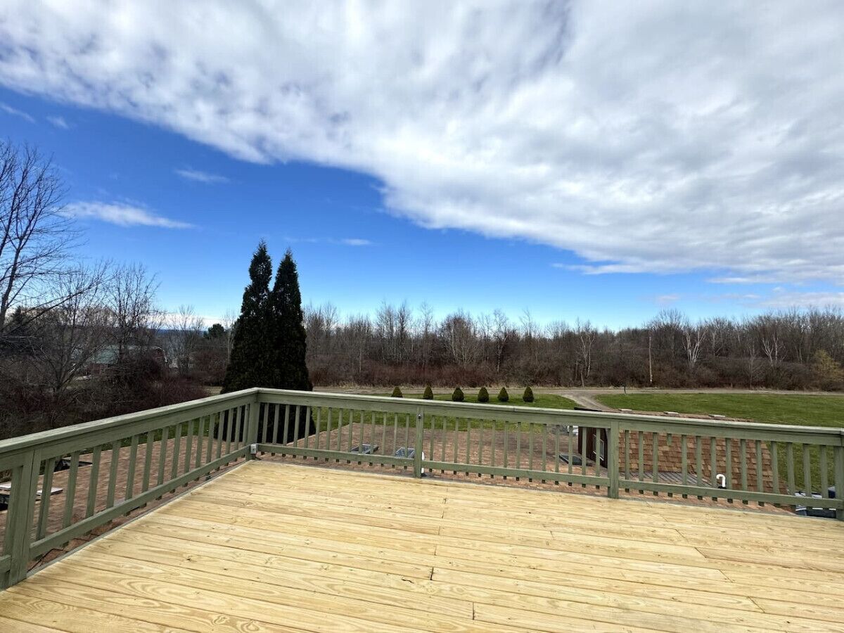 Een houten terras met een groene balustrade, met uitzicht op een gazon en bomen.