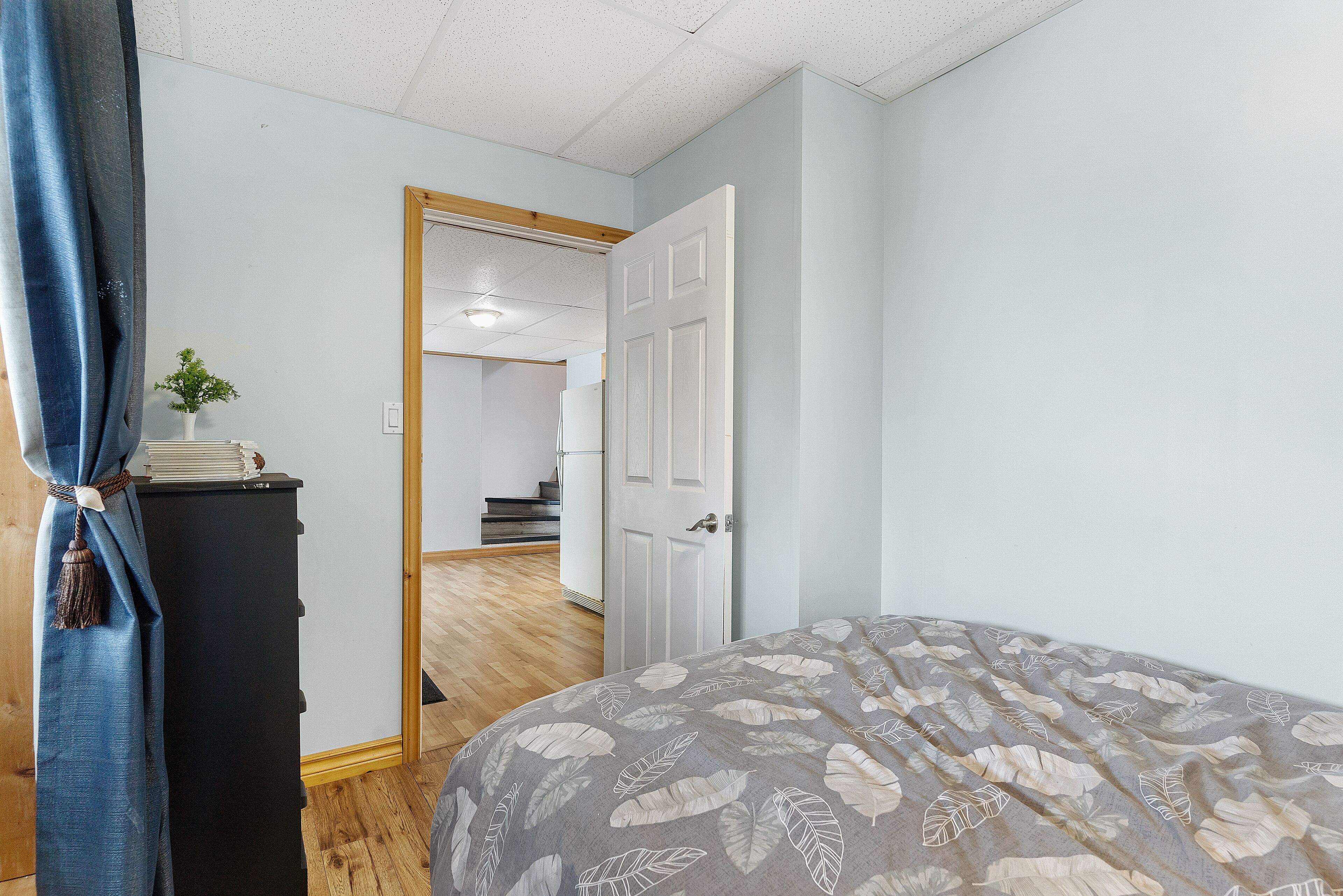 Quarto com cama, mesa de cabeceira, porta e escada que leva a outro cômodo.