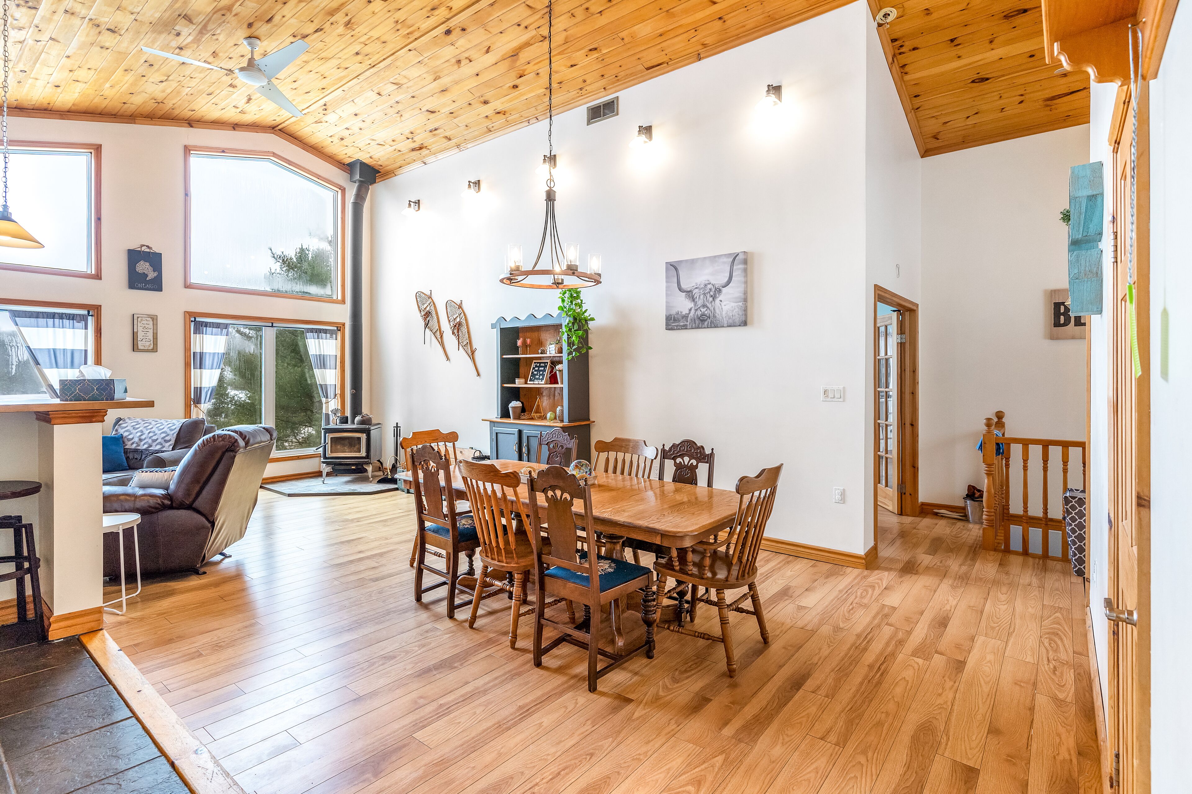A spacious dining area with a wooden table and chairs, a ceiling fan, and a view of the outdoors through large windows.