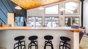 A kitchen with a wooden ceiling, large windows, and a bar area with stools.