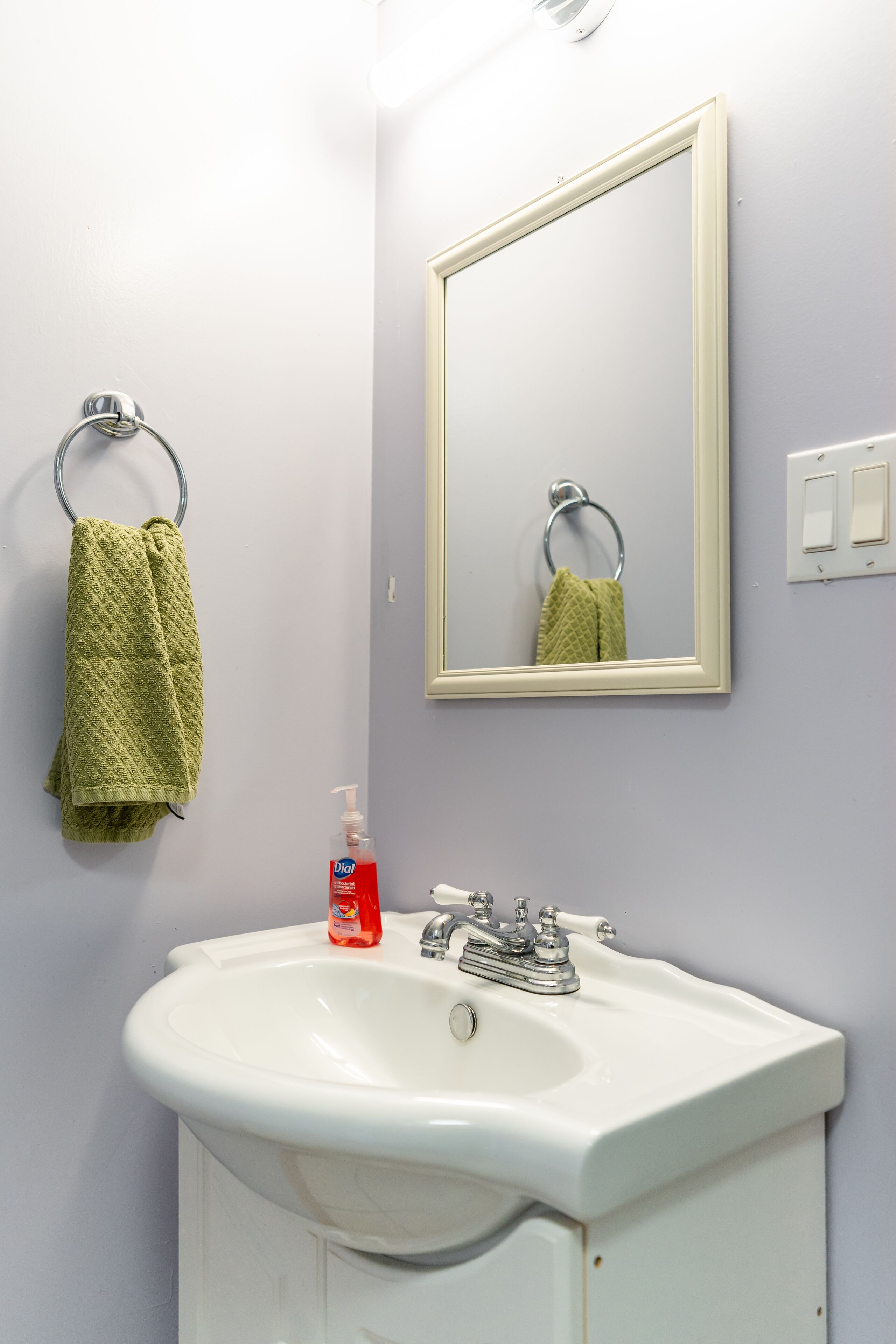 A bathroom with a white sink, a green towel, and a mirror.