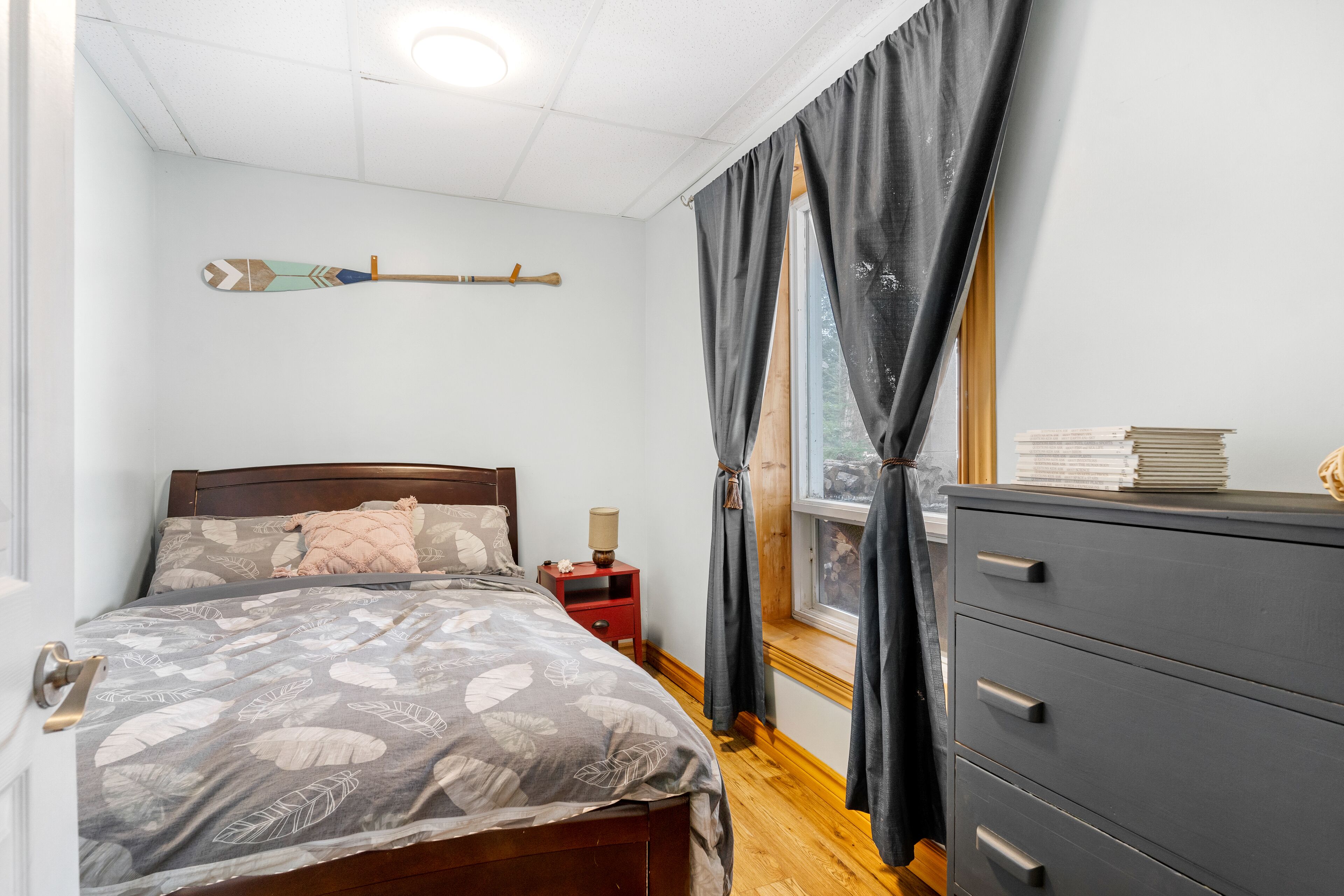 Un dormitorio con cama, mesita de noche, cómoda y ventana con cortinas.