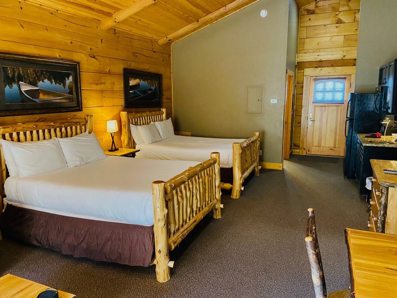 A cabin-style room with two beds, wooden furniture, and a small dining area.