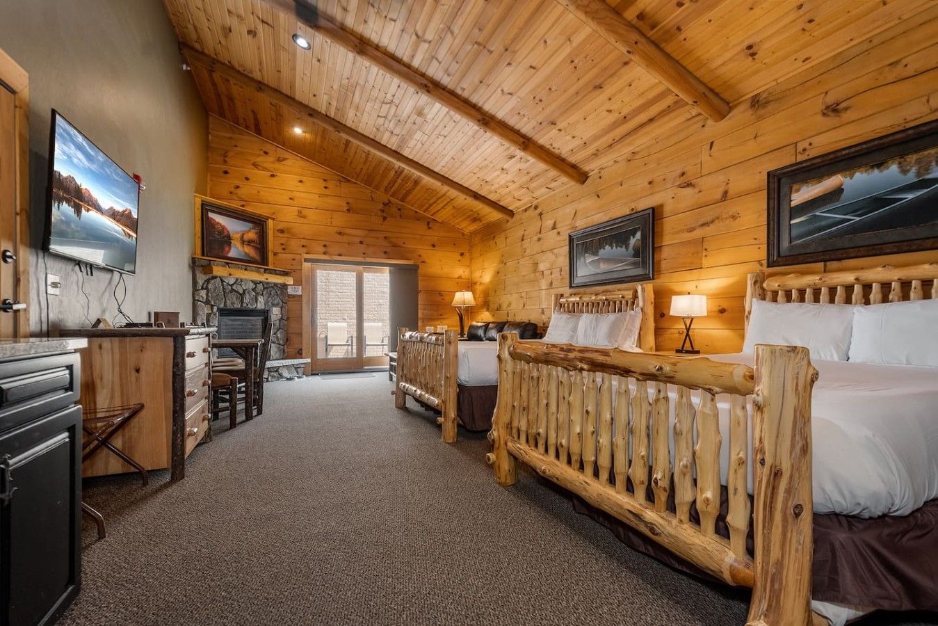 L’intérieur d’une cabane en rondins, avec une cheminée, un téléviseur et un lit doté d’une tête de lit en bois.