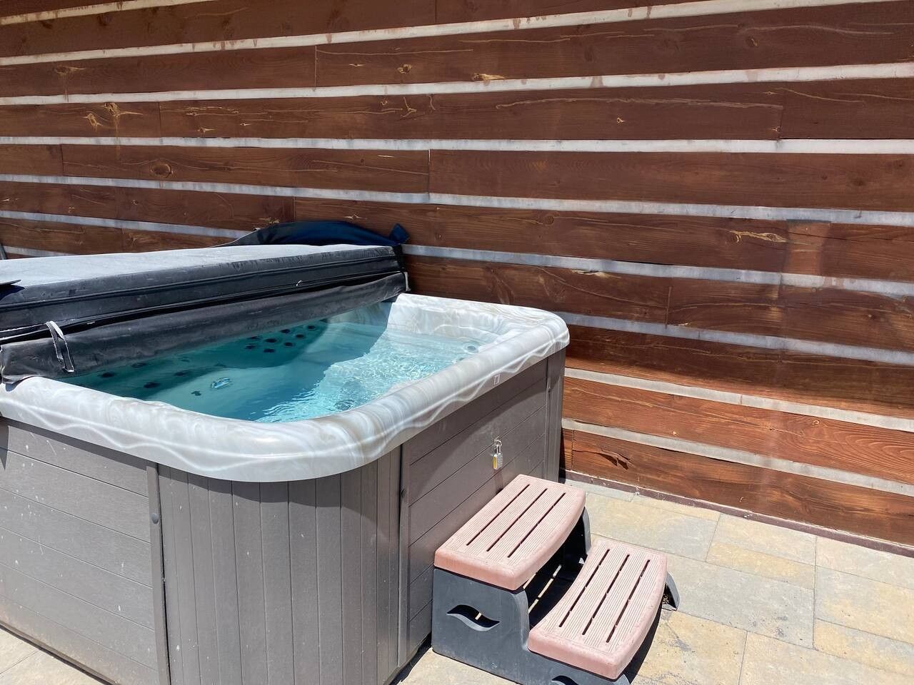 Un bain à remous avec des marches menant à celui-ci, installé contre un mur en bois.