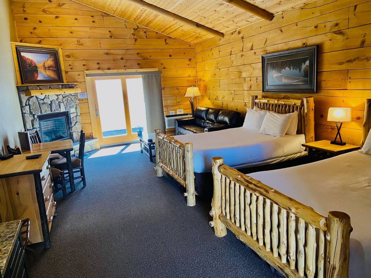A log cabin-style room with a fireplace, two beds, a dining area, and a view of the outdoors.