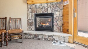 Une cheminée en pierre avec un feu, un banc en bois et une chaise rustique dans une pièce dont le mur est en pierre et la porte en bois.