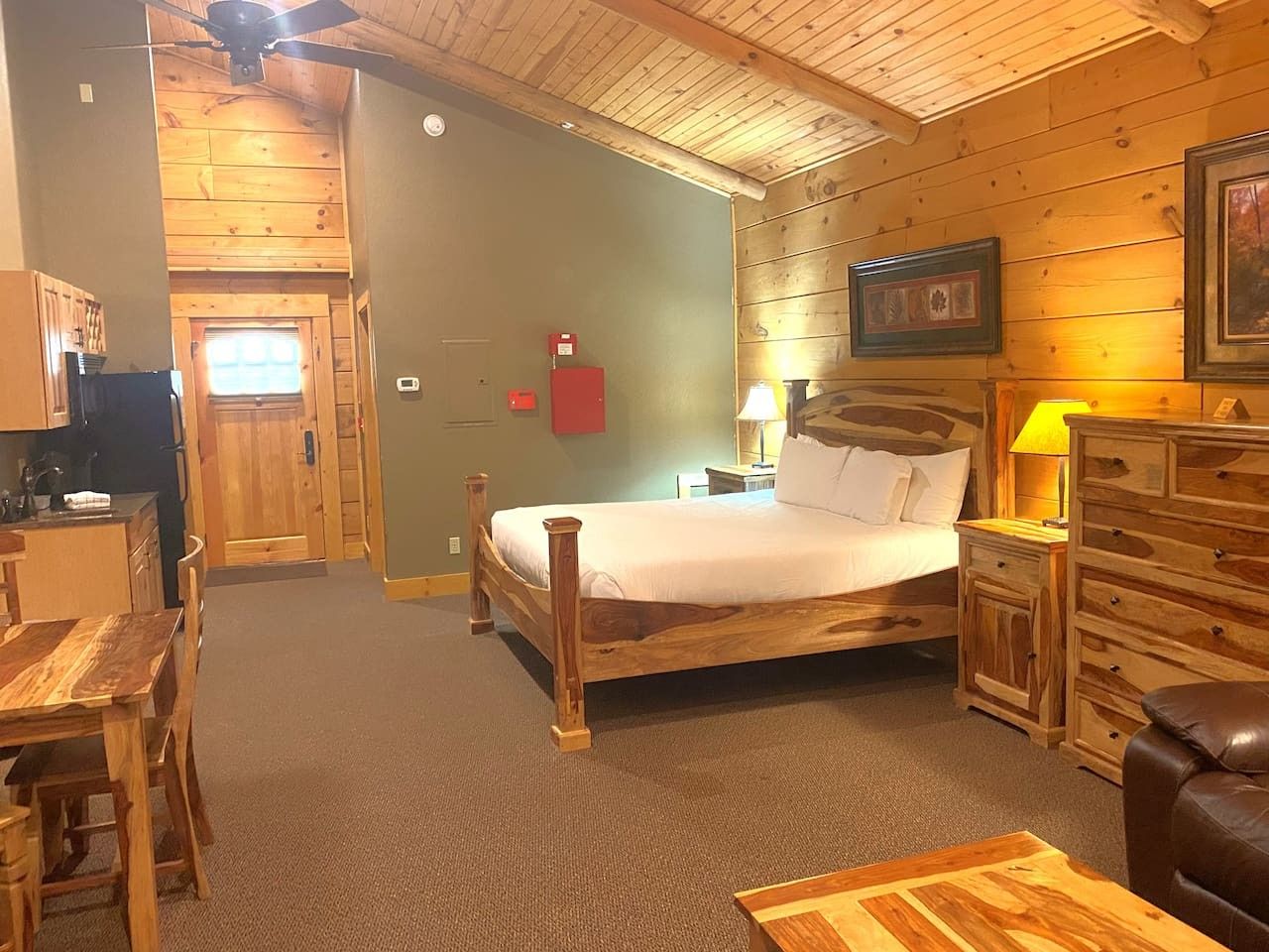 A wooden cabin interior with a bed, a dining table, and a kitchen area.