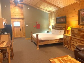 A wooden cabin interior with a bed, a dining table, and a kitchen area.