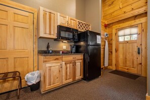 A compact kitchen with wooden cabinets, a black refrigerator, a microwave, and a coffee maker.