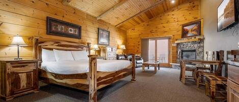 A log cabin interior with a wooden bed, a fireplace, and a dining area.