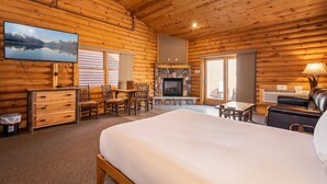 A log cabin room with a bed, a fireplace, a TV, and a dining area.
