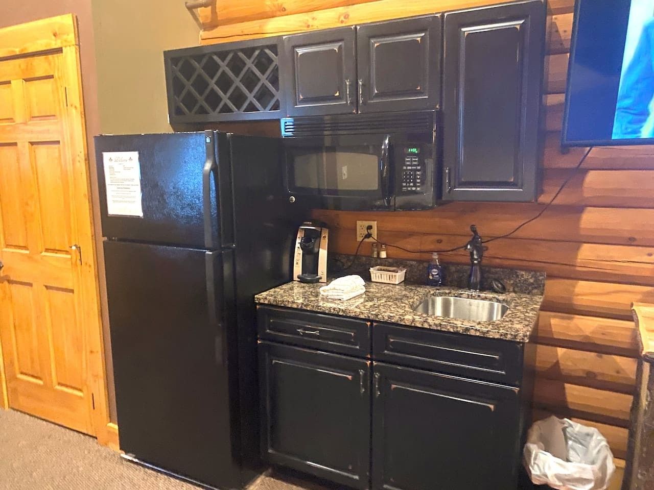 A compact kitchen with a black refrigerator, a microwave, a sink, and wooden cabinets.
