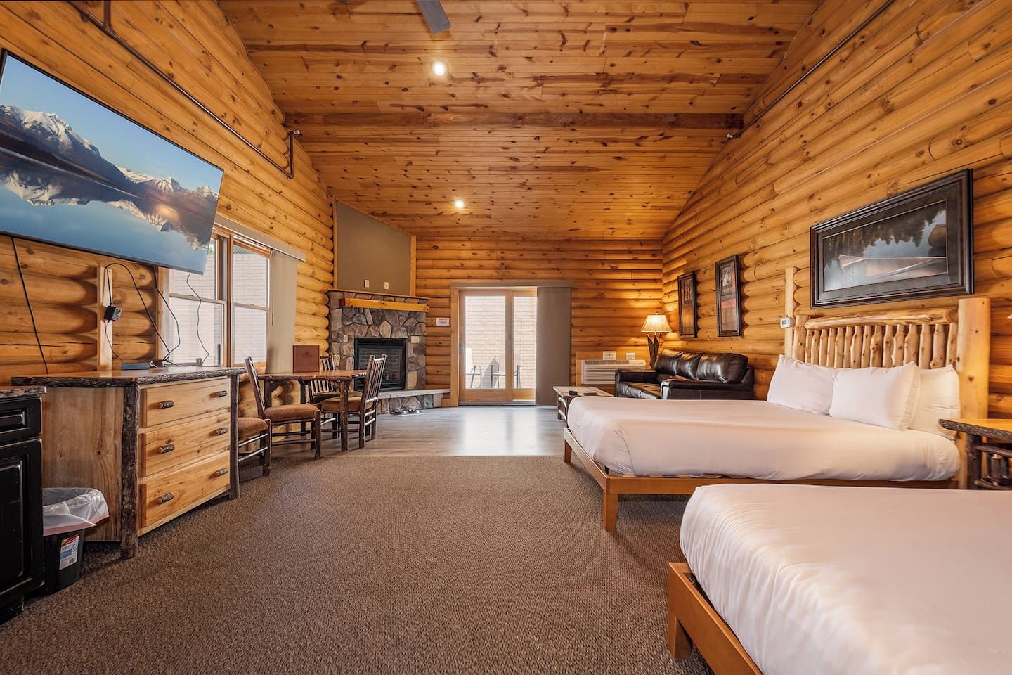 L’intérieur d’une cabane en rondins comprend un coin repas, deux lits, une cheminée et une grande fenêtre donnant sur les montagnes.