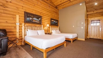 A wooden cabin room with two beds, a chair, and a lamp.