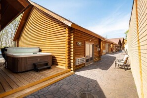 A log cabin with a hot tub, outdoor seating, and a welcoming sign.