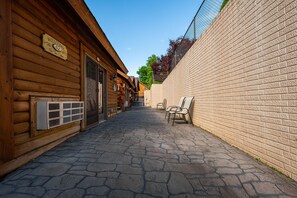 Un estrecho sendero adoquinado flanqueado por cabañas de madera y una pared de ladrillo, con un letrero que dice "Welcome to The Cabin 42".