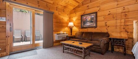 A cozy cabin interior with a wooden ceiling, a sofa, a coffee table, and a lamp.