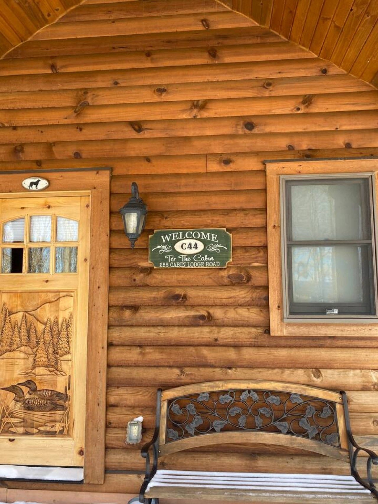 A wooden cabin with a welcome sign, a bench, and a window.