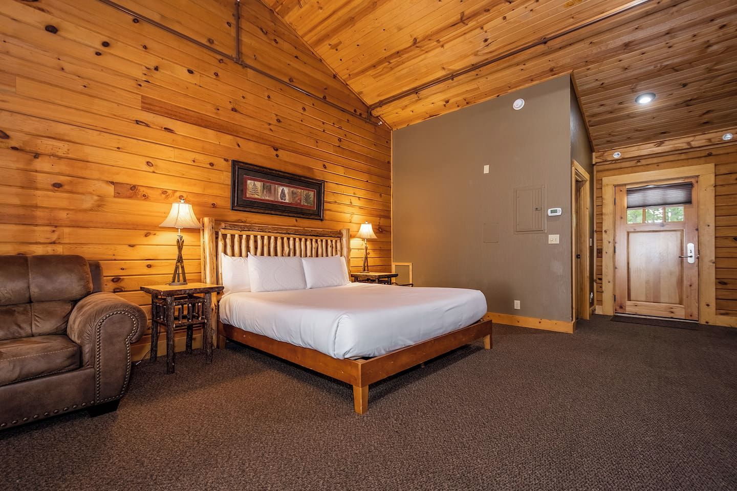 Un dormitorio de cabaña de madera con una cama, un sillón de cuero y una mesita de noche.