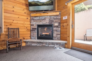 A cozy room with a stone fireplace, a television mounted above it, and a wooden chair.