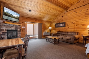 A log cabin interior with a stone fireplace, a leather sofa, a television, and a dining area.