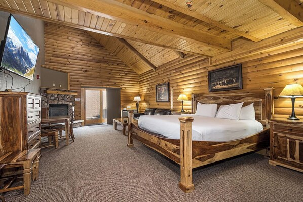 A log cabin room with a bed, a television, a fireplace, and a stone wall.