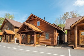 A row of log cabins with a covered front porch and a parking lot in front.