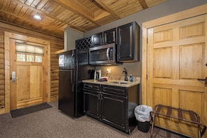 A compact kitchen with a refrigerator, microwave, and sink, wooden walls, and a door with a window.