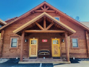 A log cabin with a pitched roof, two symmetrical doors with glass panels, and a bench in front.