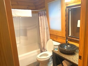 A bathroom with a toilet, a sink with a bowl, a shower curtain, and a window.