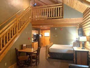 A cabin interior with a wooden staircase, a dining area, a bed, and a kitchenette.