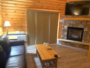 A log cabin interior with a stone fireplace, leather sofa, and a wooden table. - C45L - King, Queen, Kitchenette, Duplex (McHenry)