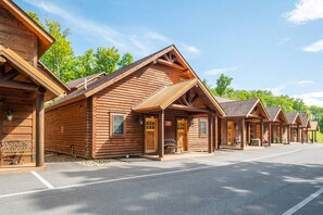 A row of log cabins with a covered porch and a paved parking area.
