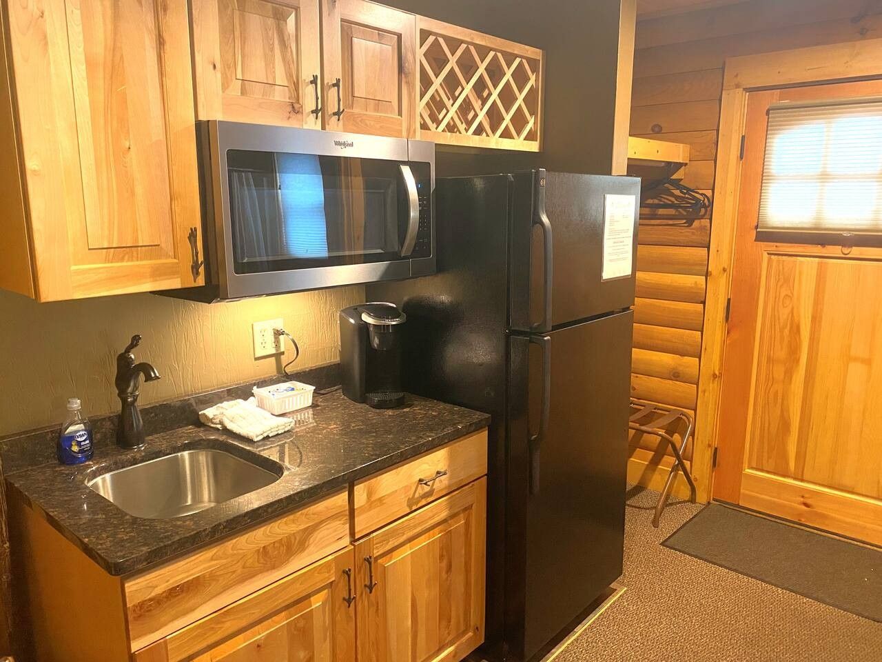 A kitchen with wooden cabinets, a stainless steel sink, a microwave, a refrigerator, and a coffee maker.