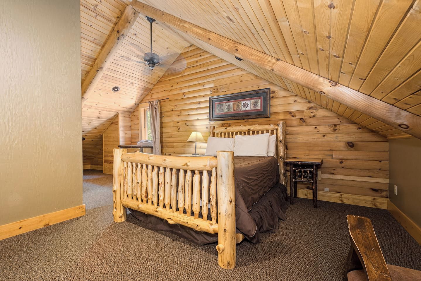 A cozy attic bedroom with a wooden bed, a nightstand, and a ceiling fan.