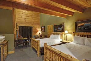 A room with two wooden beds, a dining table with chairs, a small table with a lamp, and a painting on the wall.