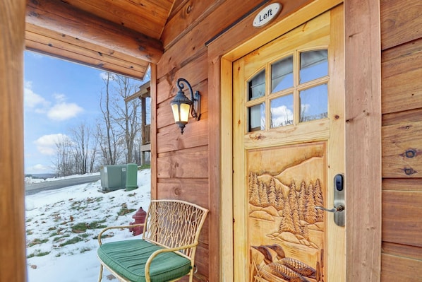 A wooden cabin with a carved door, a bench, and a street view outside.