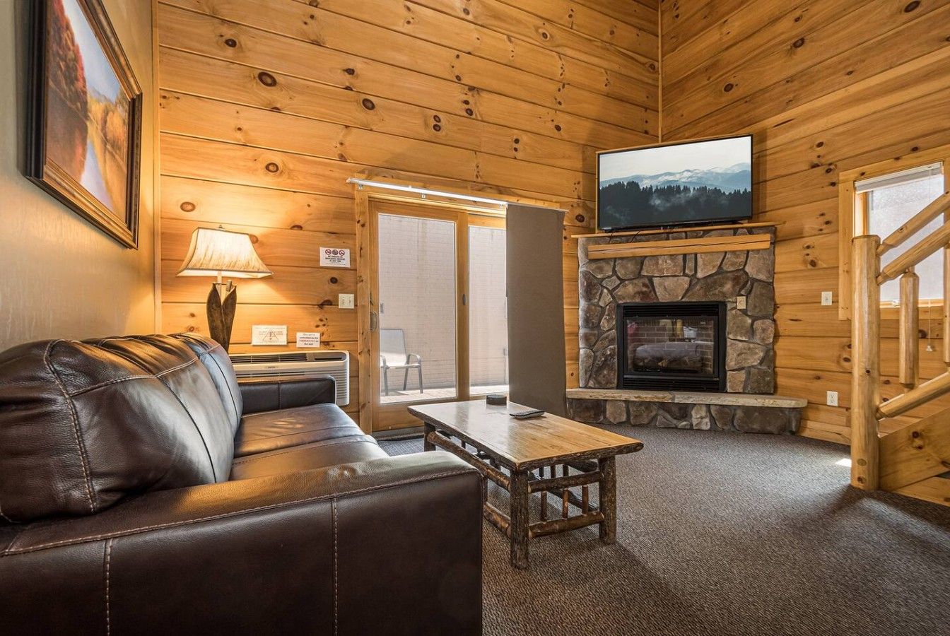 A cozy cabin interior with a stone fireplace, leather sofa, and a television mounted above it.