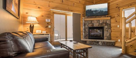 A cozy cabin interior with a stone fireplace, leather sofa, and a television mounted above it.