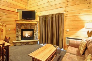 A cozy cabin interior with a stone fireplace, a television mounted above it, a sofa, and a table.